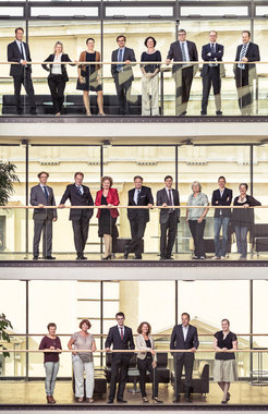 Gruppen von Personen stehen auf drei Stockwerken eines verglasten Gebäudes.